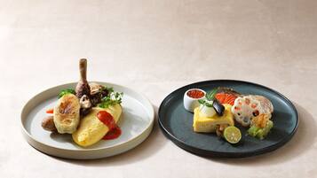 Two plates of food with various dishes including a grilled item, a fish, and a small bowl of sauce.