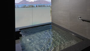 Ein modernes Badezimmer mit einer gläsernen Whirlwanne, klarem Wasser und Blick auf Berge und Bäume.