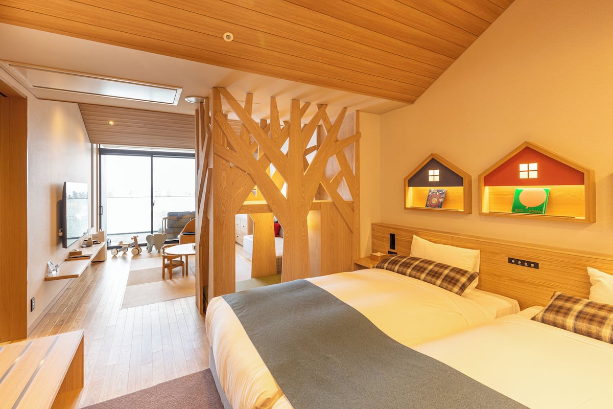 Habitación de hotel moderna con una cama grande, techo de madera y vistas a la ciudad a través de un ventanal amplio.