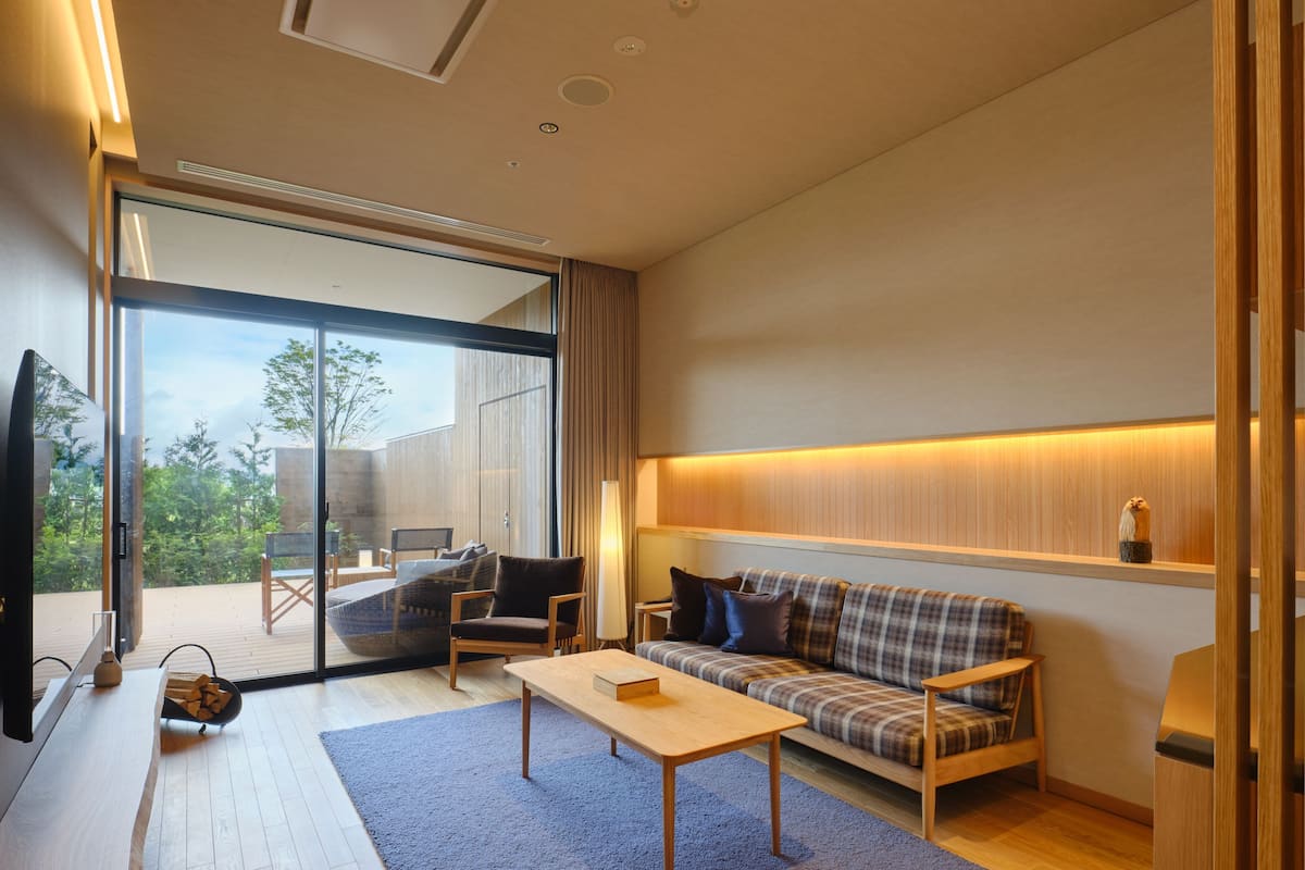 Una sala moderna con un sofá, una mesa de centro y un televisor. Hay una puerta corrediza de vidrio que da a un área exterior con una terraza.