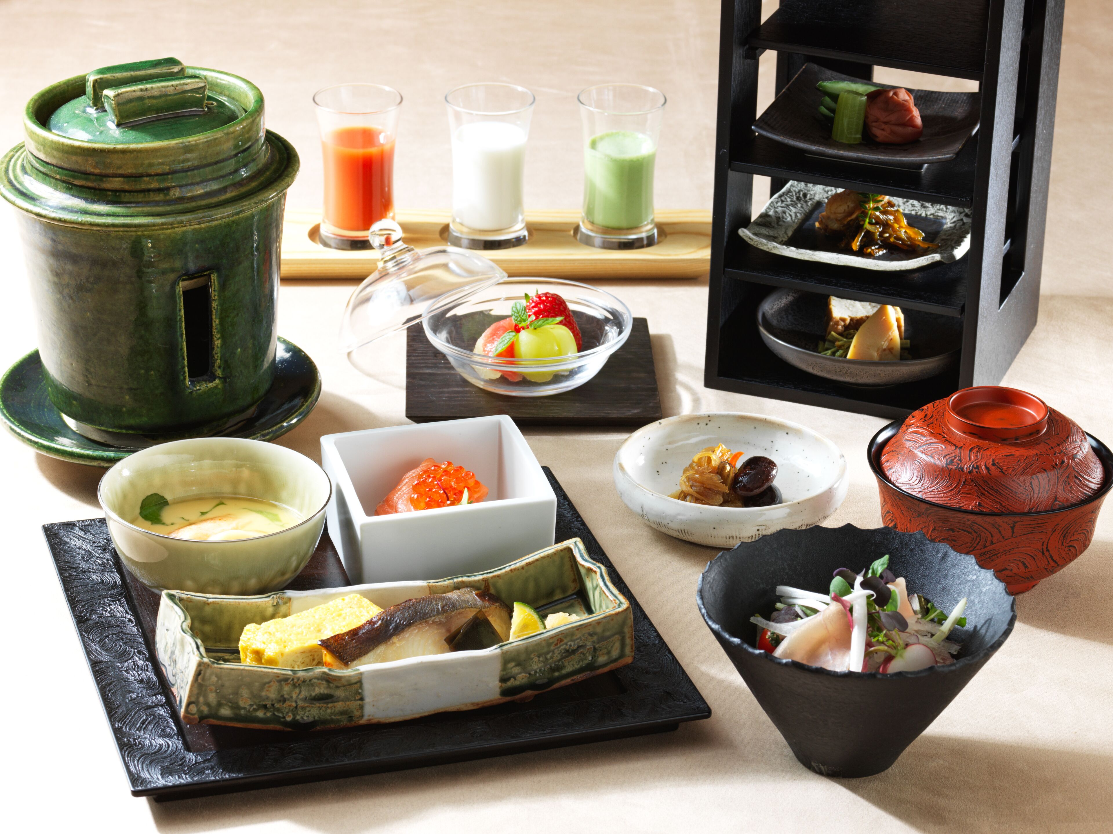 A variety of dishes and drinks, including a green teapot, a bowl of soup, and a plate with vegetables.