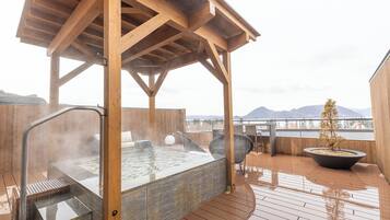 A wooden deck with a hot tub, a seating area, and a view of mountains.