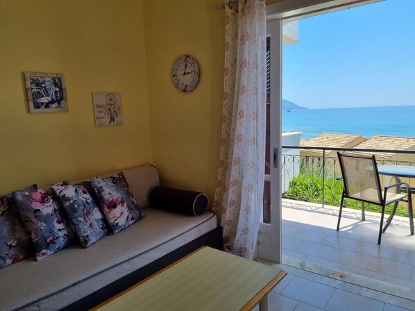 A room with a sofa, a table, and a view of the sea.