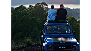 Two people in a blue SUV with a Jeep logo, parked on a road with a sunset in the background. - a very interesting tour held on top of Mount Batur, 4wd jeeps tour (Bali)