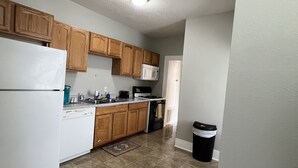 A kitchen with wooden cabinets, a white refrigerator, a microwave, a stove, and a trash can. - Historical Spacious 1-Bedroom Apartment Unit 3 (Shreveport)