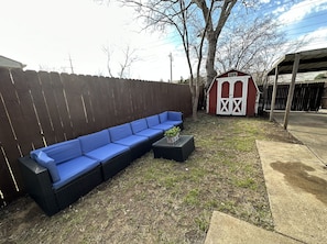 A backyard with a blue sectional sofa, a small shed, and a covered patio area.