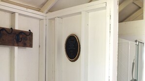 A small, enclosed space with a wooden bench, a plaque on the wall, and a glass door leading to a shower area. - Tent Platform 3 | Pond View Glamping Tent (Latah County)