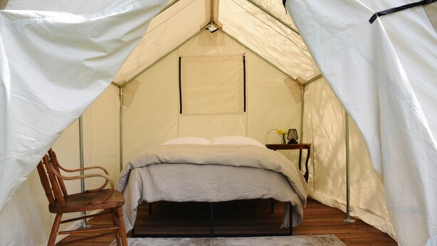 A tent with a bed, a chair, and a small table with a lamp. - Tent Platform 3 | Pond View Glamping Tent (Latah County)