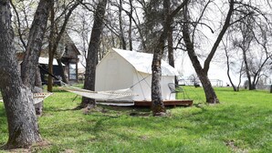 A tent-like structure with a hammock and a small table, surrounded by trees and a grassy field. - Tent Platform 3 | Pond View Glamping Tent (Latah County)