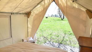 A tent with a bed inside, a view of a grassy field, and a wooden dresser. - Tent Platform 4 | Pond View Glamping Tent (Latah County)