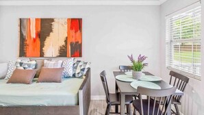 Una habitación moderna con una cama, una mesa de comedor con sillas y un cuadro abstracto grande en la pared.