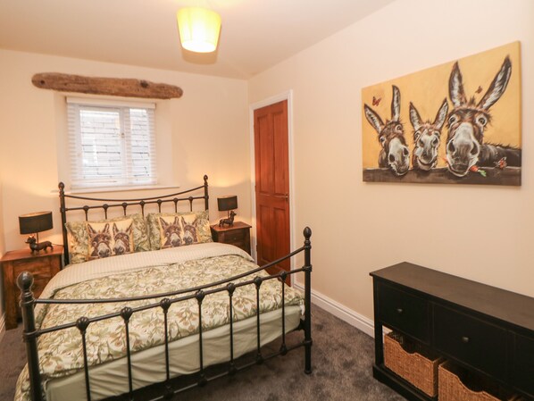 A bedroom with a bed, two bedside tables, a nightstand, a lamp, a window with blinds, a door, and a painting on the wall.