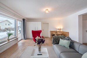 Ein modernes Wohnzimmer mit einem roten Sessel, einem grauen Sofa und einer Blumenvase auf einem weißen Couchtisch.