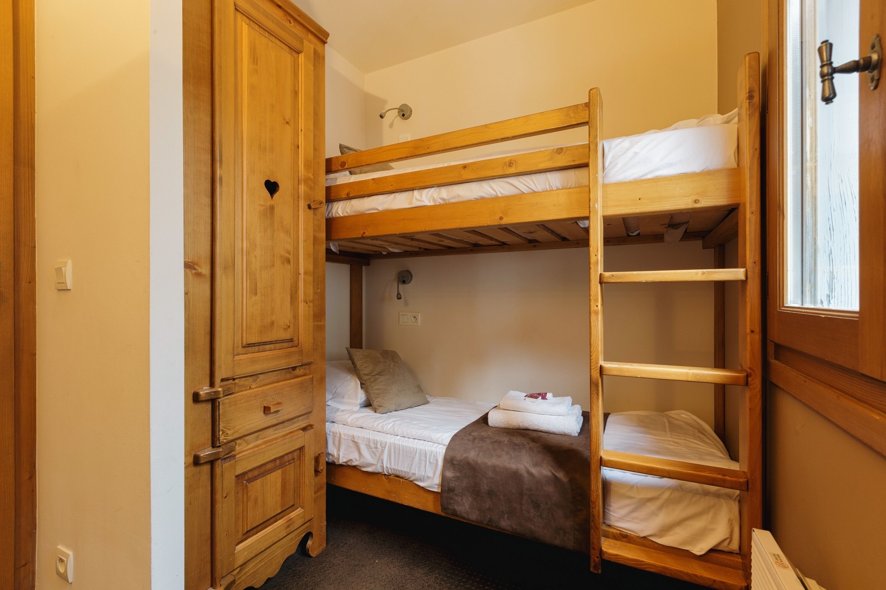 Een slaapkamer met een stapelbed, een houten garderobe en een raam.