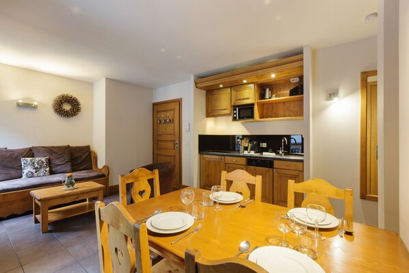 A dining area with a wooden table set for four, a kitchen with wooden cabinets, and a living area with a sofa and a coffee table. - Vallorcine Buet 33 ski in / ski out, Vallorcine (Argentiere), France (Vallorcine (Argentiere))