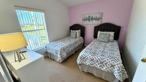 A bedroom with two beds, a desk, a lamp, and a cityscape painting on the wall.
