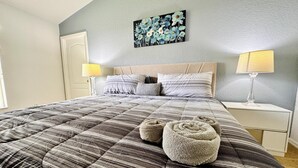 A neatly made bed with striped bedding, two bedside lamps, and a floral artwork on the wall.