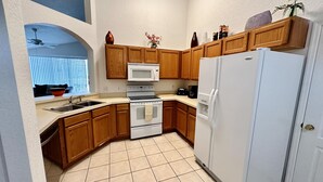A compact kitchen with wooden cabinets, a white refrigerator, a microwave, an oven, and a sink.