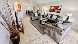 A spacious living room with a sofa set, a coffee table, and a dining area with chairs and a table.
