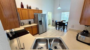 Una cocina con armarios de madera, un refrigerador de acero inoxidable, un lavamanos doble y un comedor con mesa y sillas.