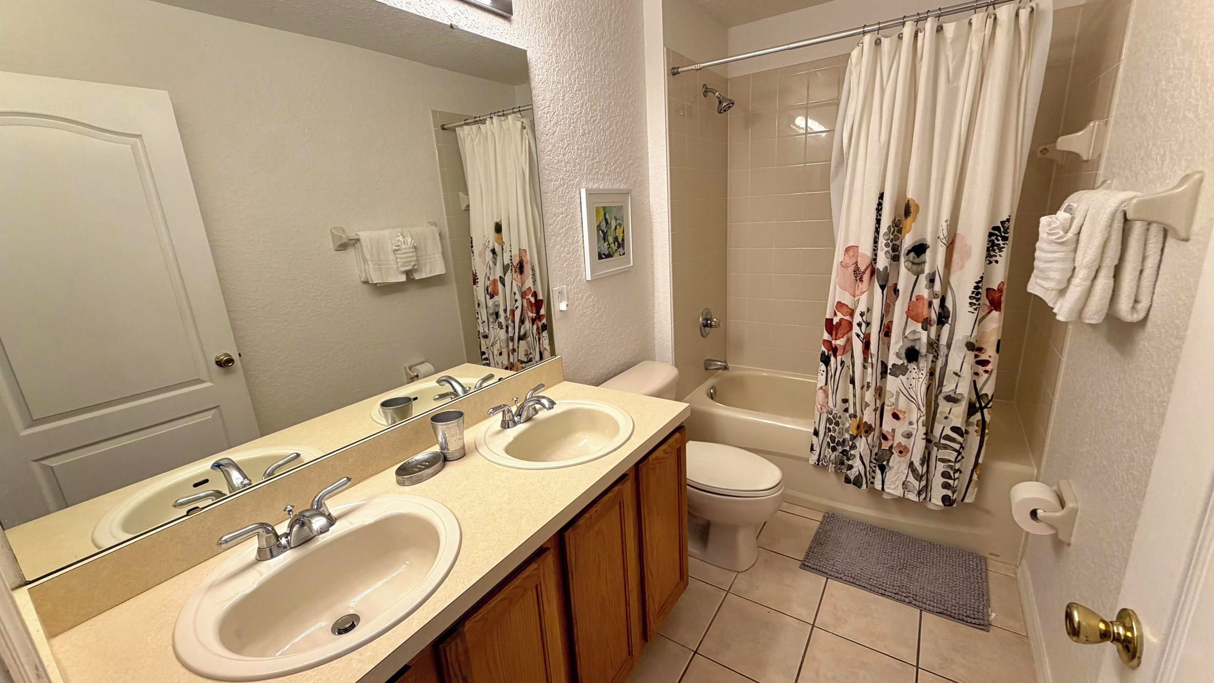 A bathroom with two sinks, a toilet, a shower with floral curtains, and a towel rack.