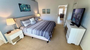 Un dormitorio con una cama, mesitas de noche, una lámpara, un televisor y obras de arte en las paredes.