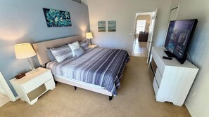 A bedroom with a bed, nightstands, a lamp, a TV, and artwork on the walls.