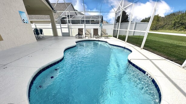 A swimming pool with a curved edge, surrounded by a covered patio area with chairs and a fence.