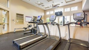 Centre de fitness amb cintes de córrer, una màquina d'a rem i un televisor fixat a la paret.