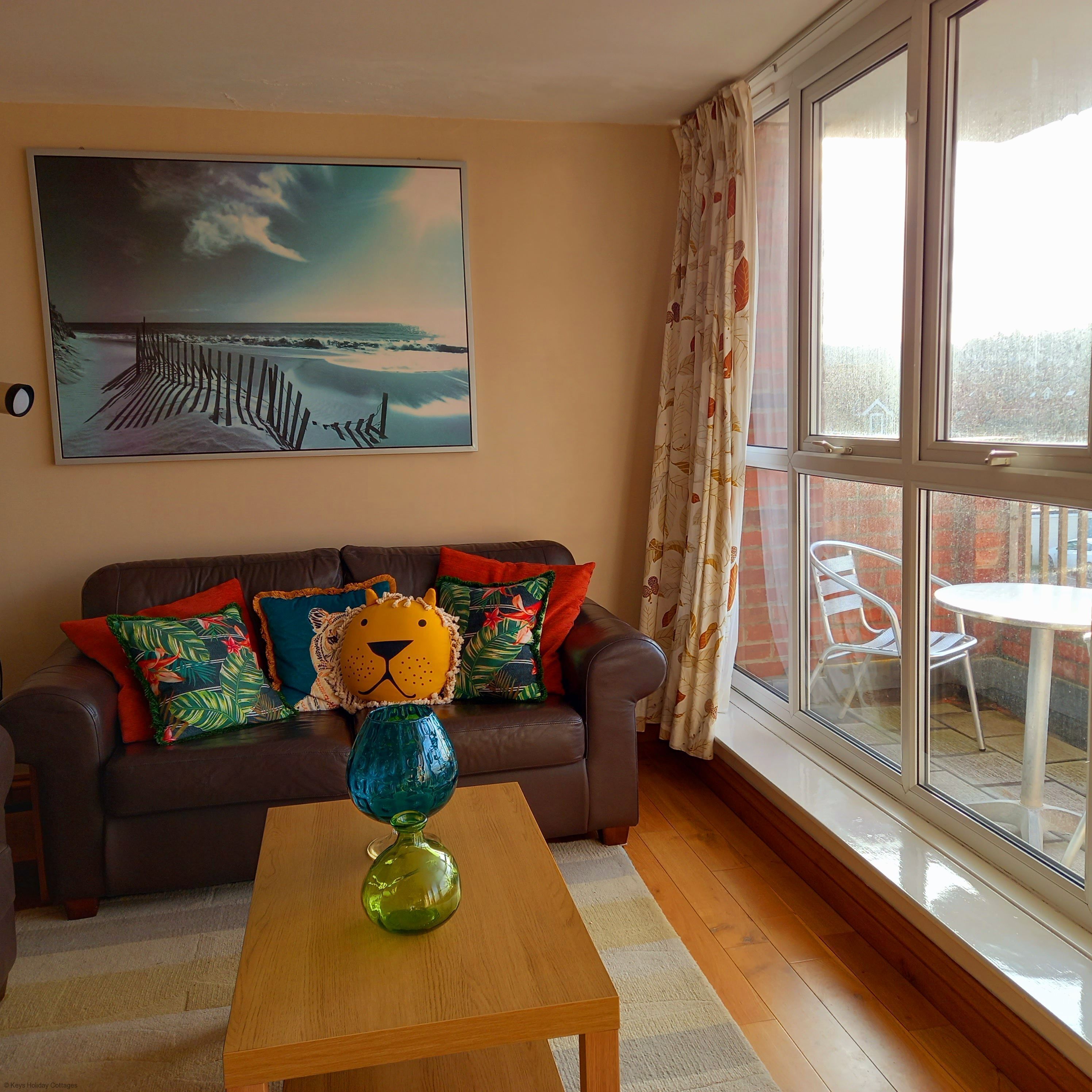 A living room with a sofa, a glass coffee table, a painting, and a view through a window.