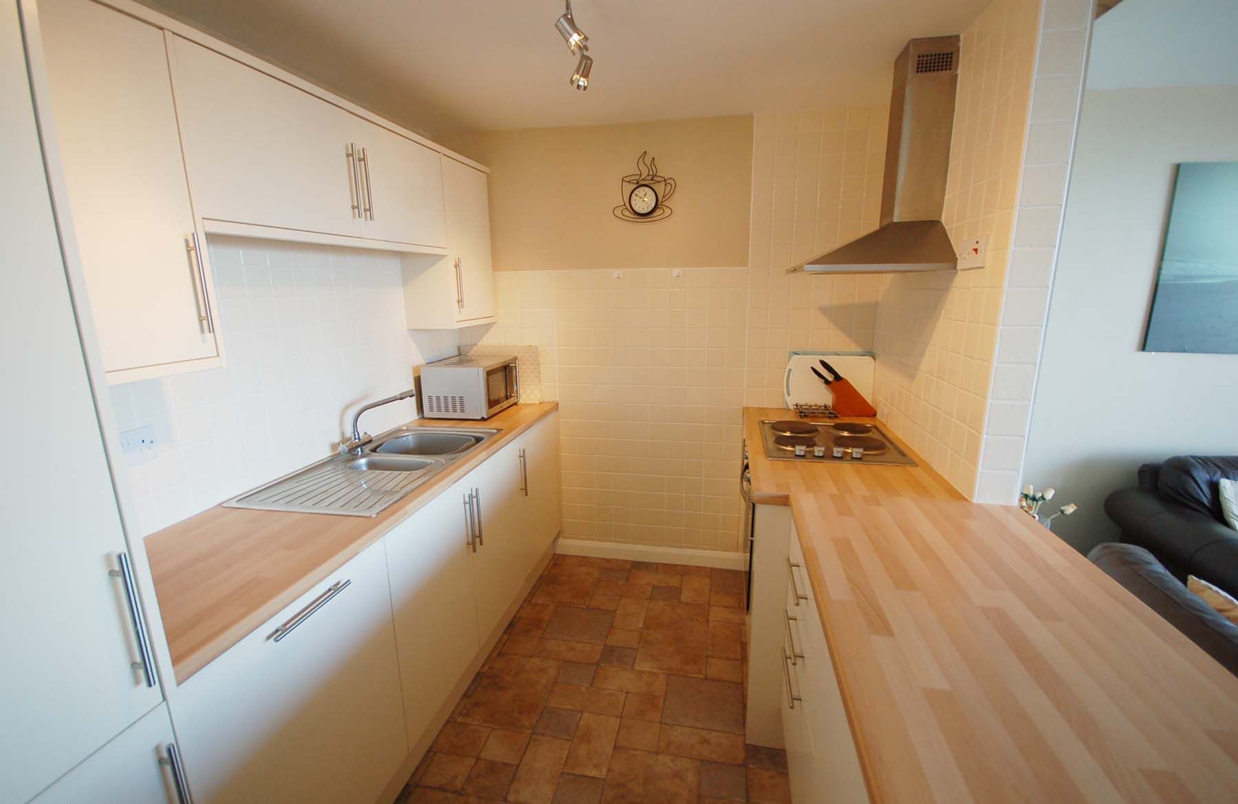 Cocina compacta con armarios blancos, microondas, estufa y lavaplatos.
