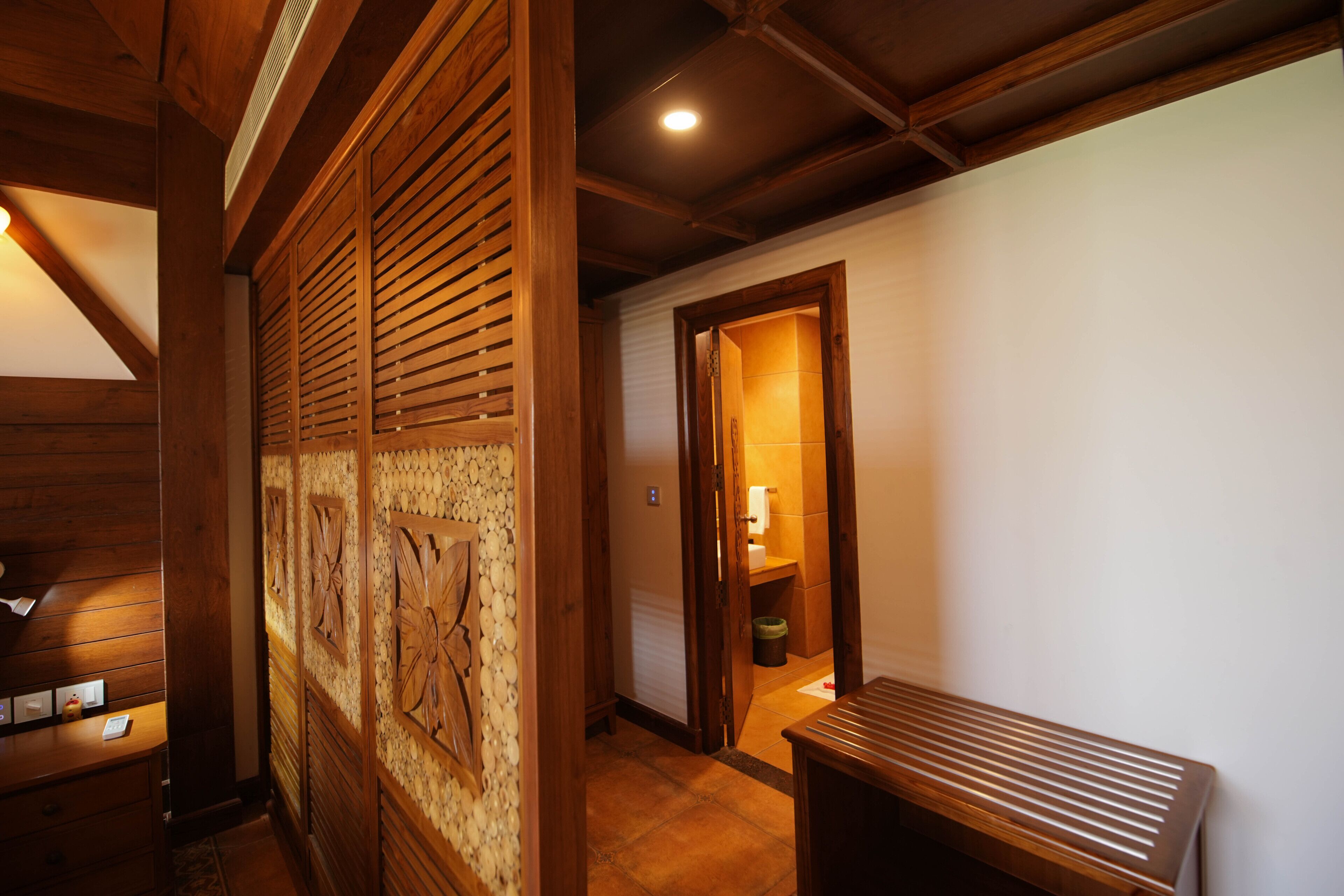 A wooden interior with a bench, a door leading to a lit room, and a wall with a decorative panel.