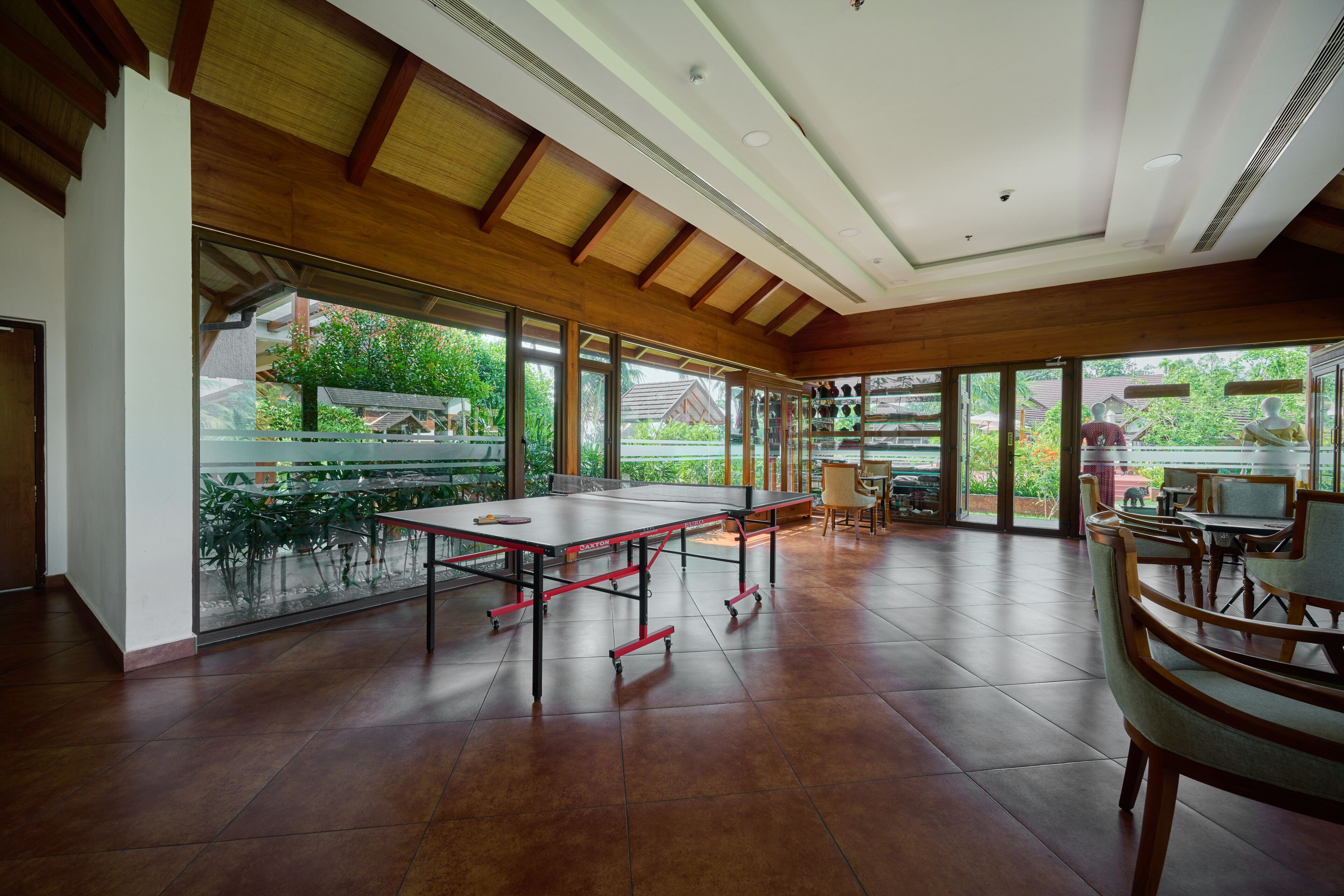 A spacious room with a ping pong table, large windows, and a view of greenery outside.