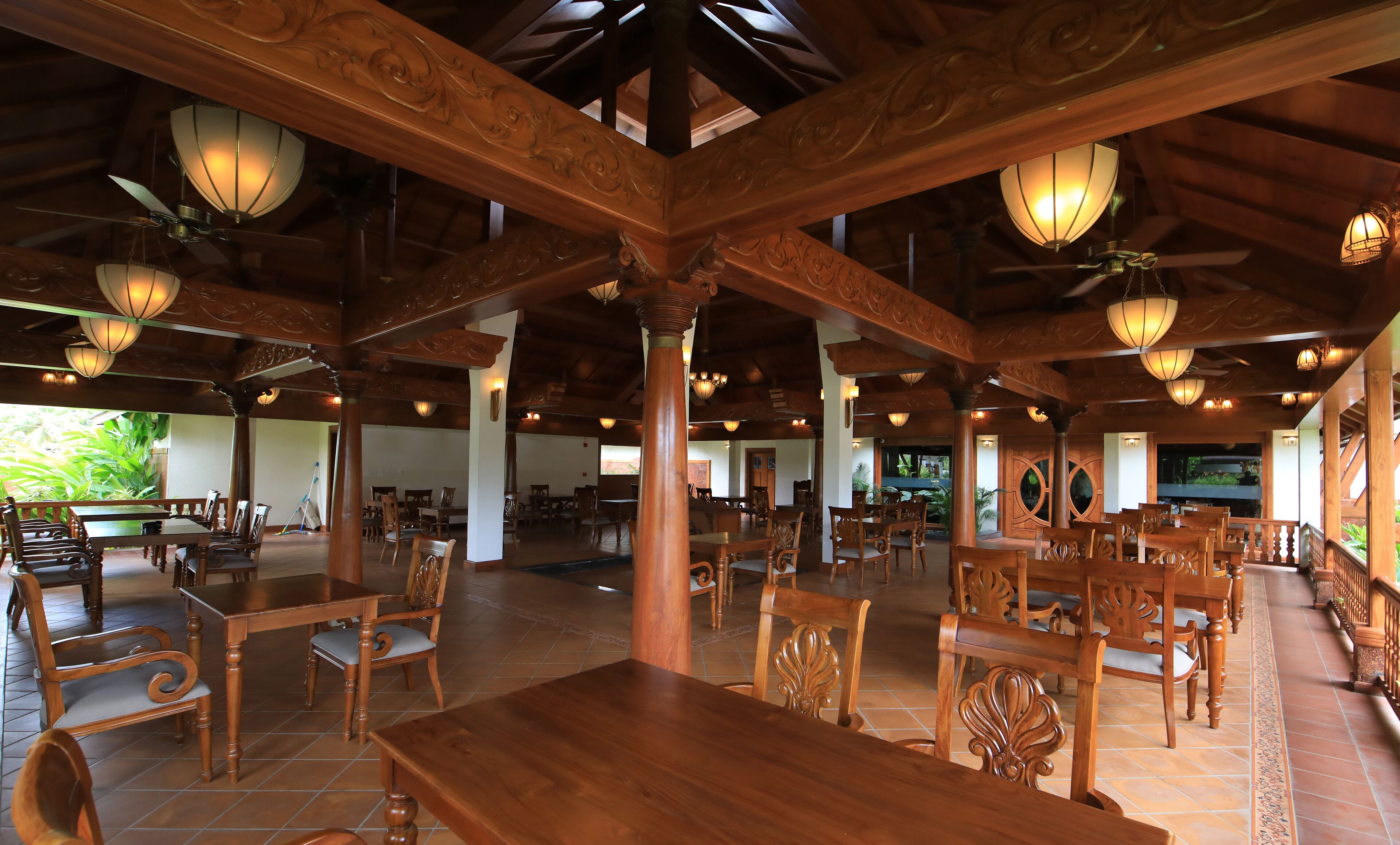 A spacious indoor area with wooden tables and chairs, large columns, and hanging light fixtures.