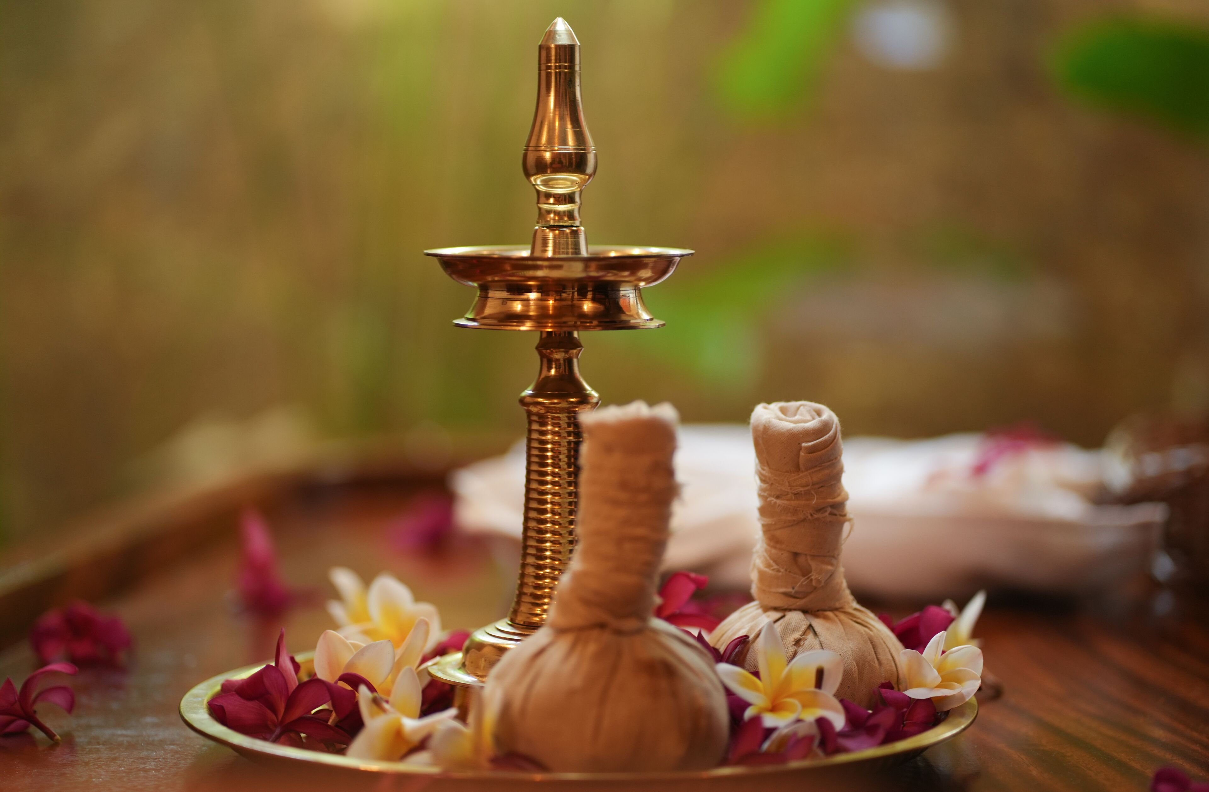 A brass oil lamp, two rolled-up mats, and a plate with flowers on a wooden surface.
