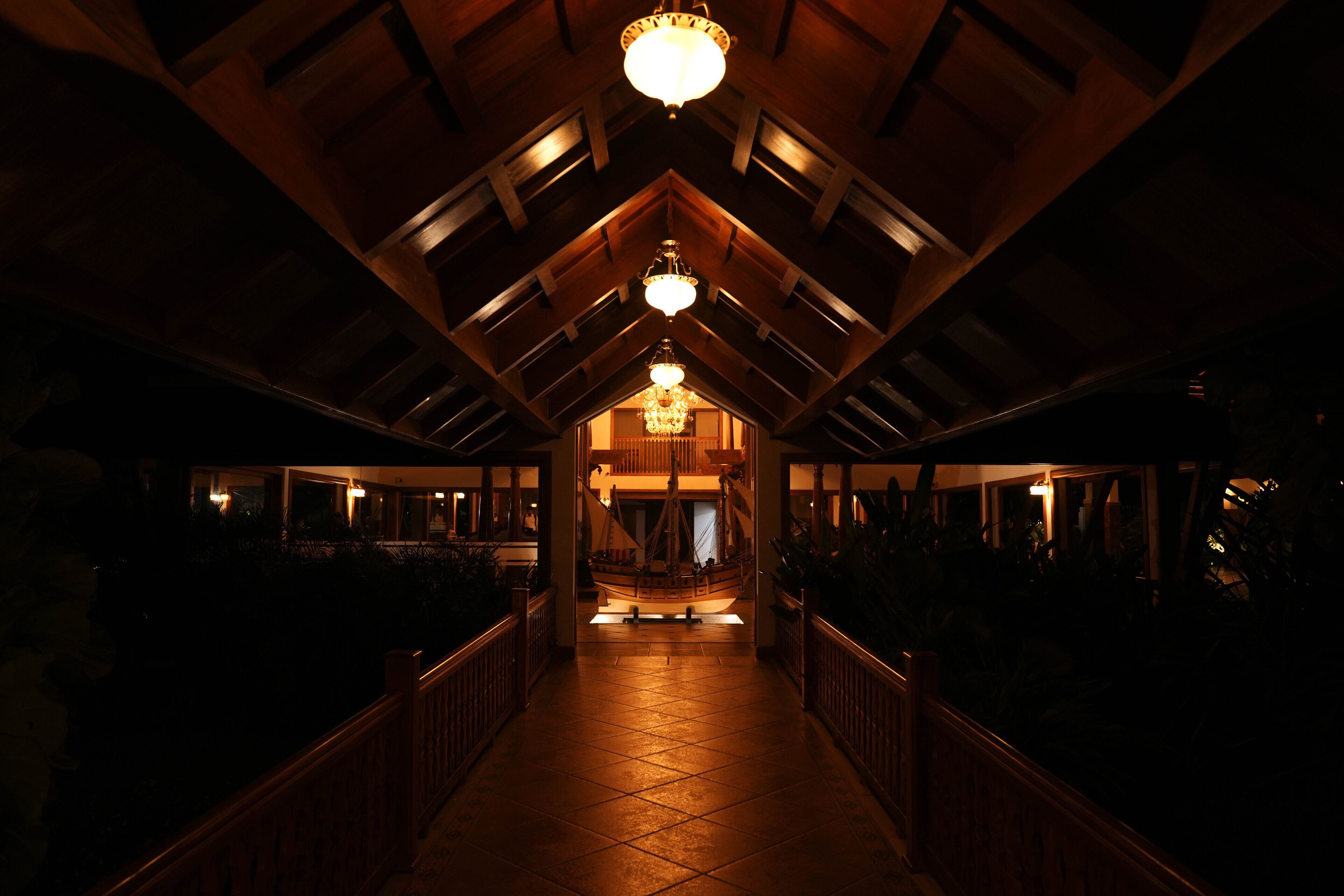 A corridor with a wooden railing, a chandelier, and a boat model in the center.