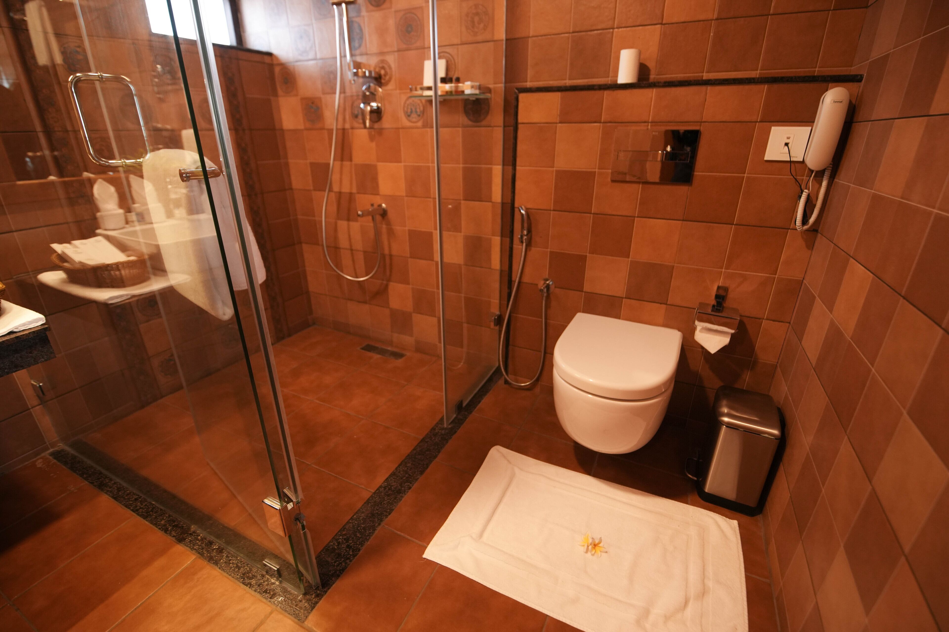 Un baño con cabina de ducha de vidrio, inodoro, lavabo y un cubo de basura.