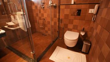 Un baño con cabina de ducha de vidrio, inodoro, lavabo y un cubo de basura.