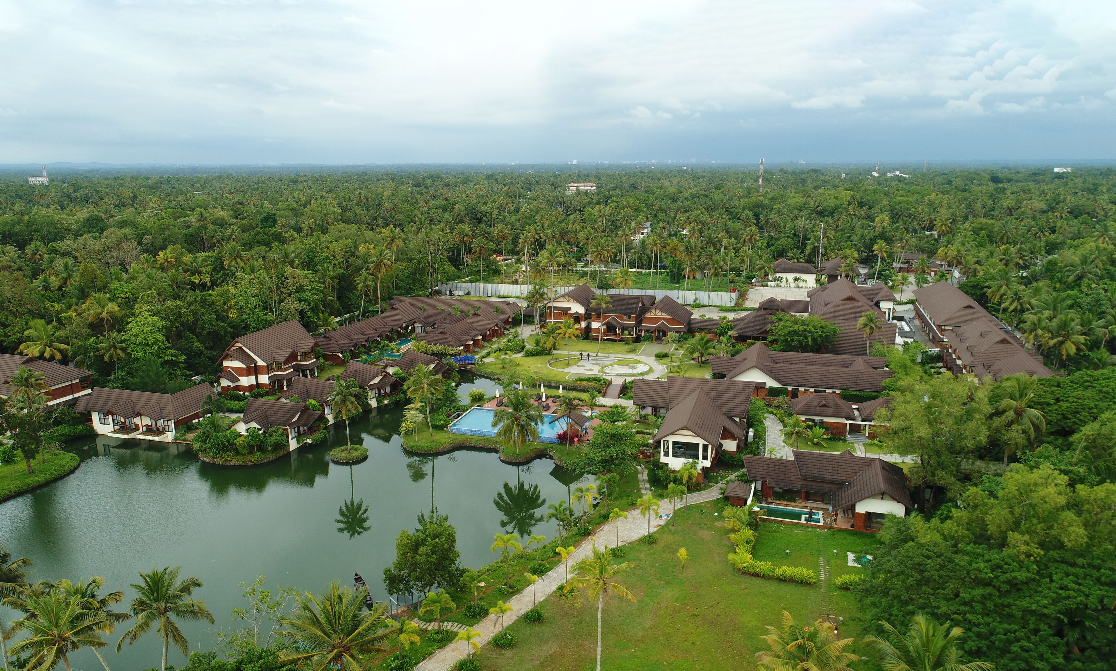 A resort with multiple bungalow-style buildings, a central swimming pool, and a surrounding natural landscape.