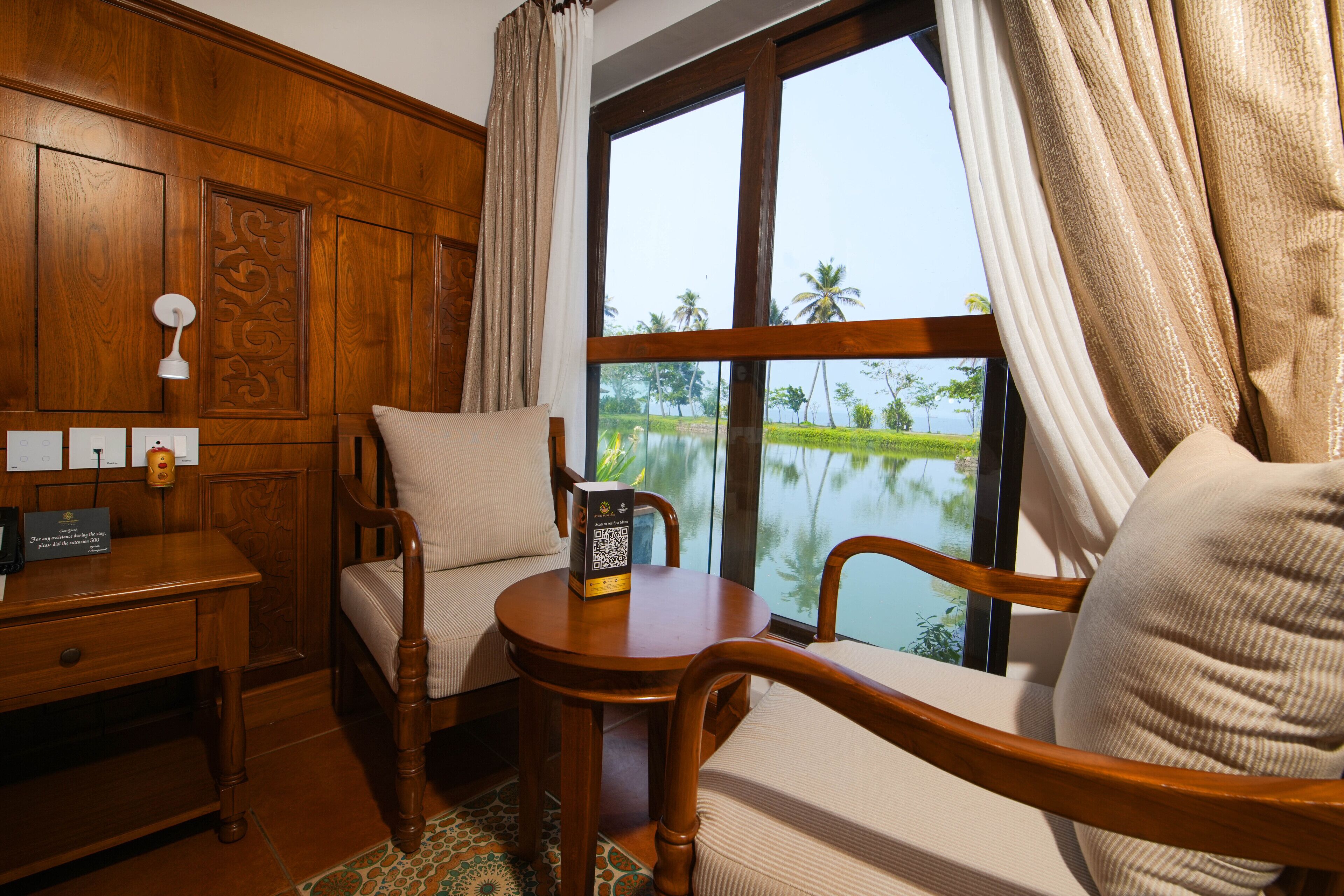 A wooden room with a view of a lake, a desk with a lamp, and two chairs.