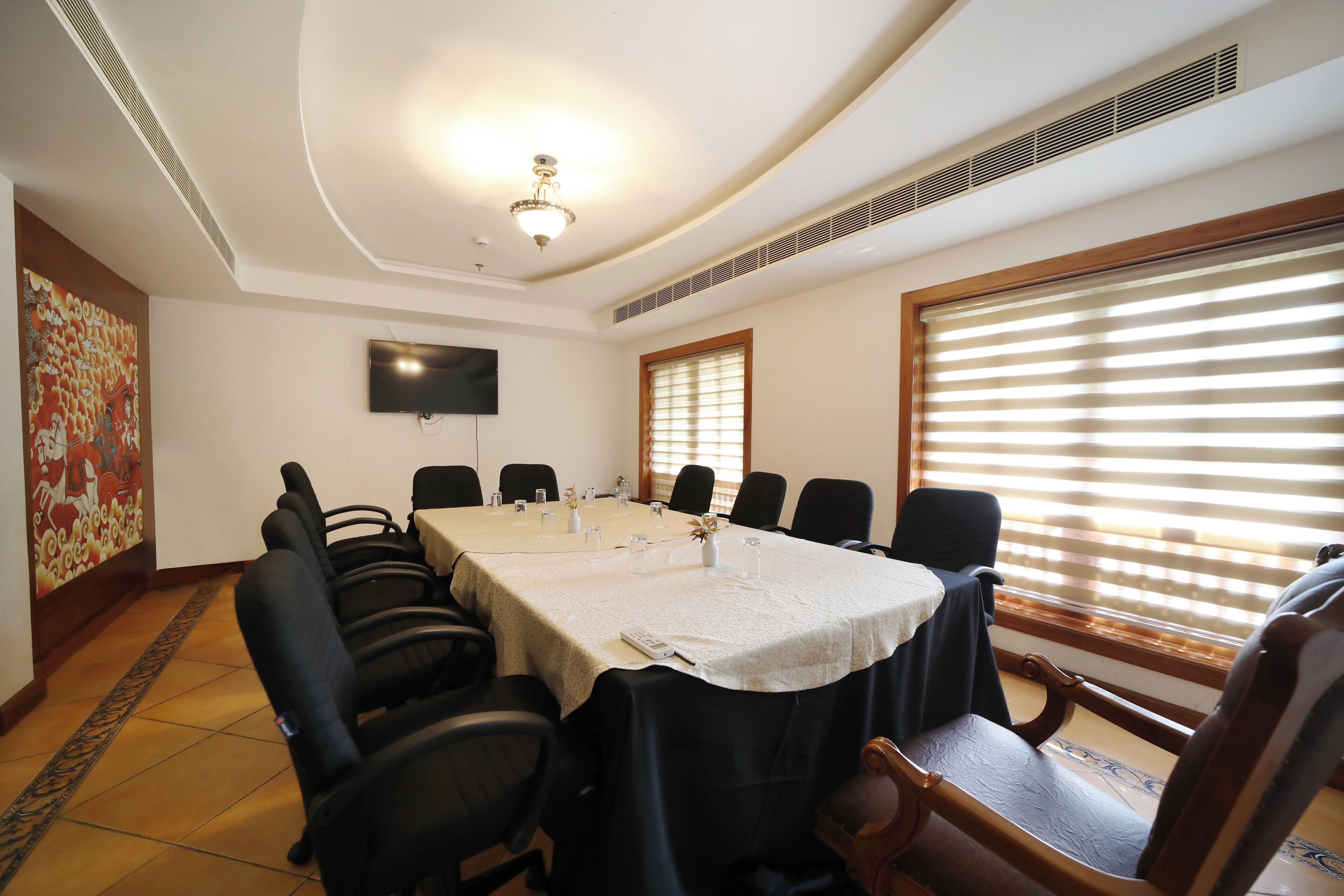 A conference room with a long table, chairs, a TV on the wall, and a window with blinds.