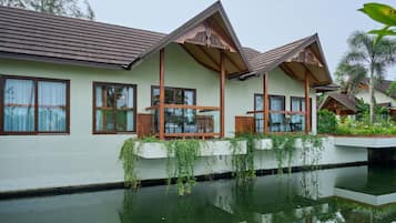 Een resort met een groot wateroppervlak ervoor, houten balkons en een lichtgekleurde gevel.