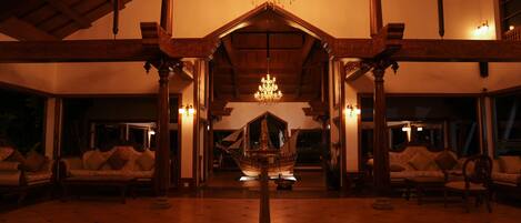 A lobby with a chandelier, wooden columns, and a ship model.