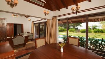 A dining area with a wooden table and chairs, a vase of flowers, and a view of a swimming pool and garden.