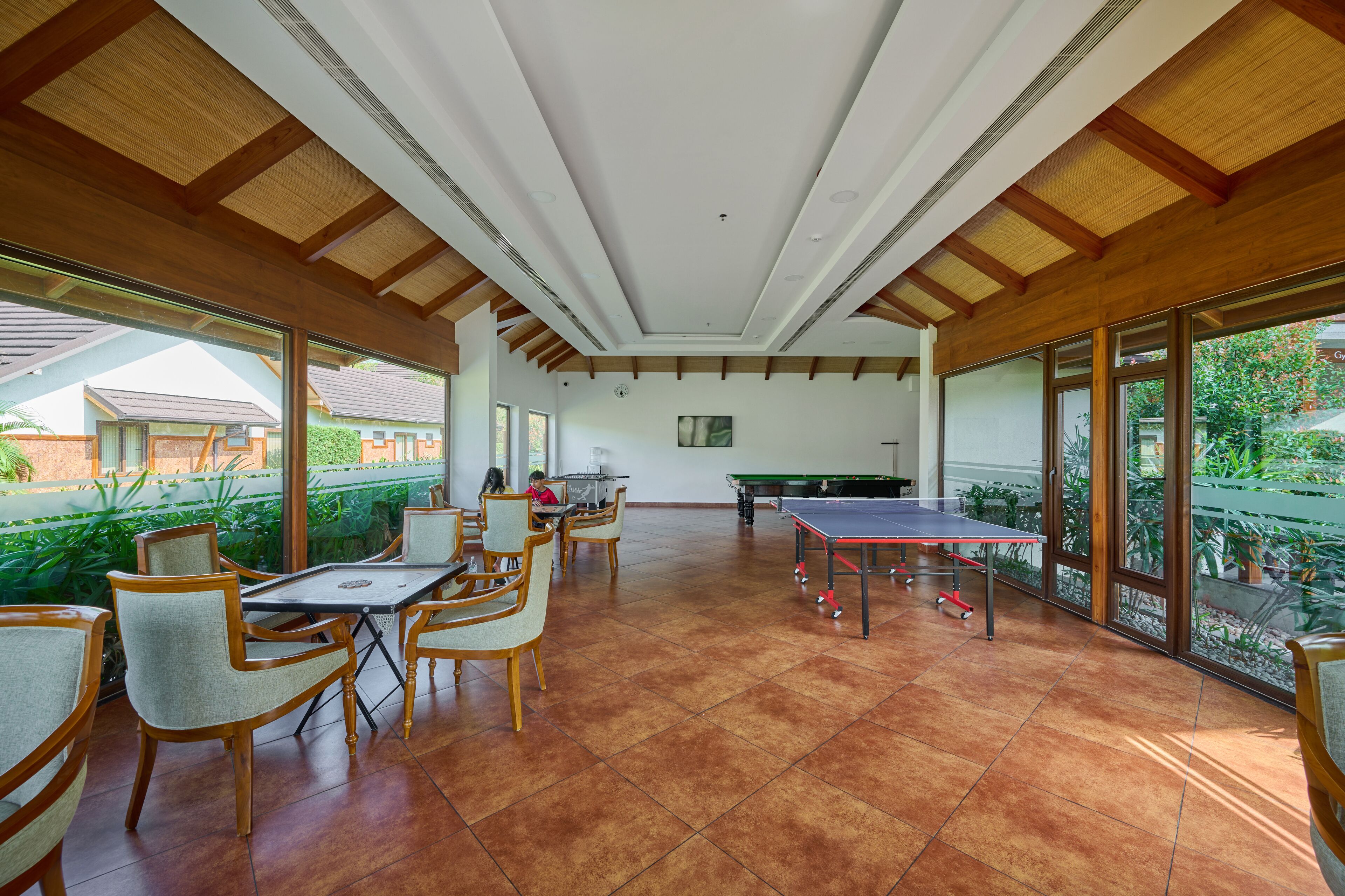A spacious indoor area with a ping pong table, wooden chairs, and large windows offering views of the outside.