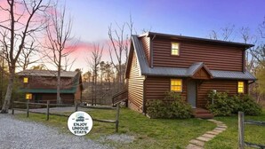 A two-story log cabin with a front porch and a small attached structure.