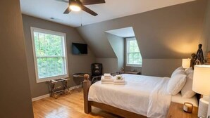 A bedroom with a bed, ceiling fan, wooden floor, and a window.