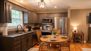A kitchen with dark cabinets, stainless steel appliances, a wooden dining table, and a chandelier.