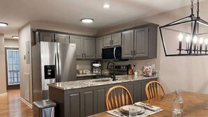 Una cocina moderna con gabinetes grises, electrodomésticos de acero inoxidable, encimera de granito y un comedor con mesa y sillas de madera.