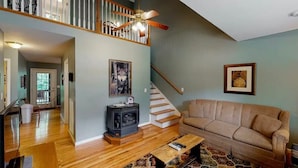 A spacious living room with a wooden floor, a beige sofa, a patterned rug, a fireplace, and a staircase with a railing. - The Loose Moose with a private hot tub! (Rising Fawn)